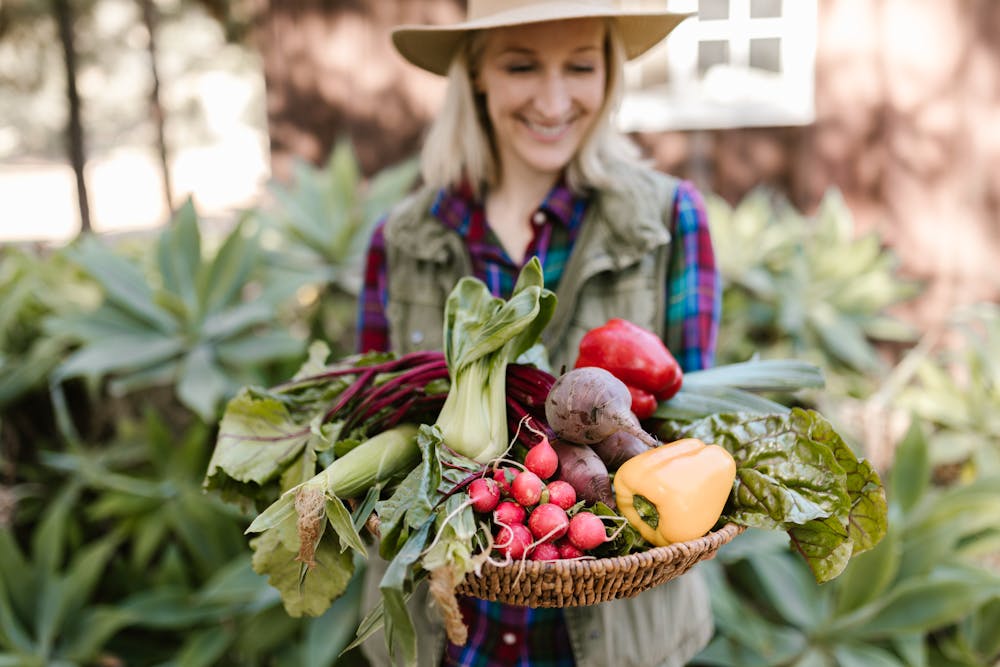 a woman holding a basket full of fresh vegetables from her garden